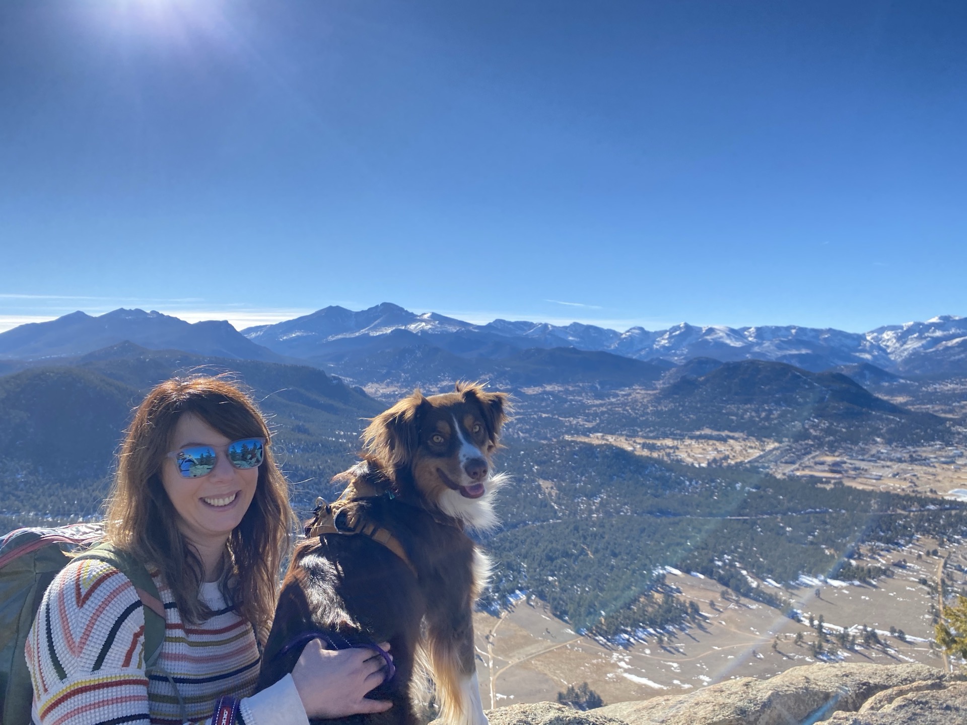 A hiker with a dog on a summit overlooking the Rockies