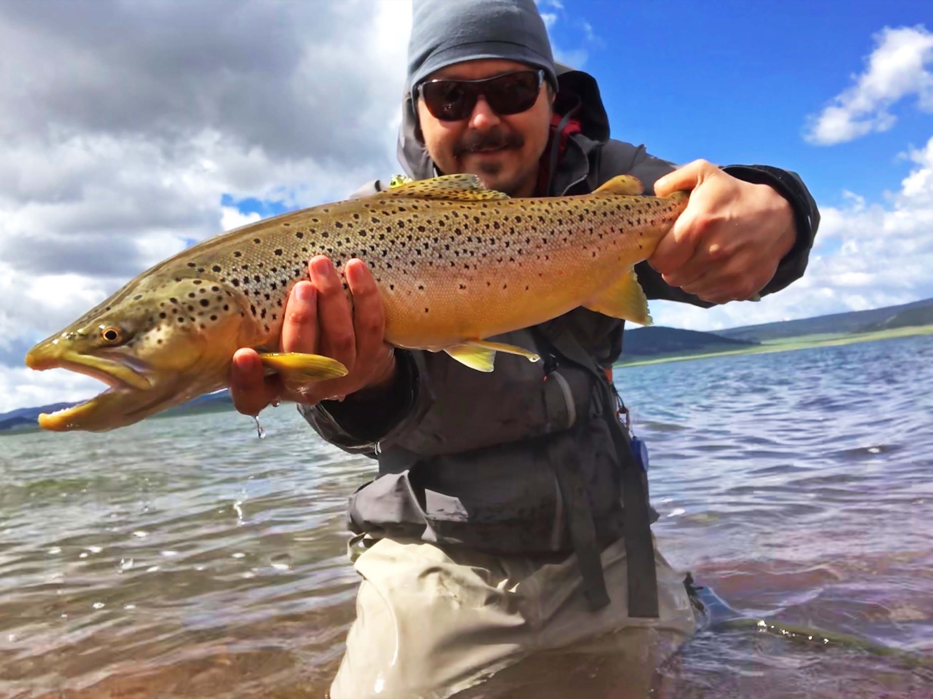 A smiling guide in sunglasses holding a golden brown trout